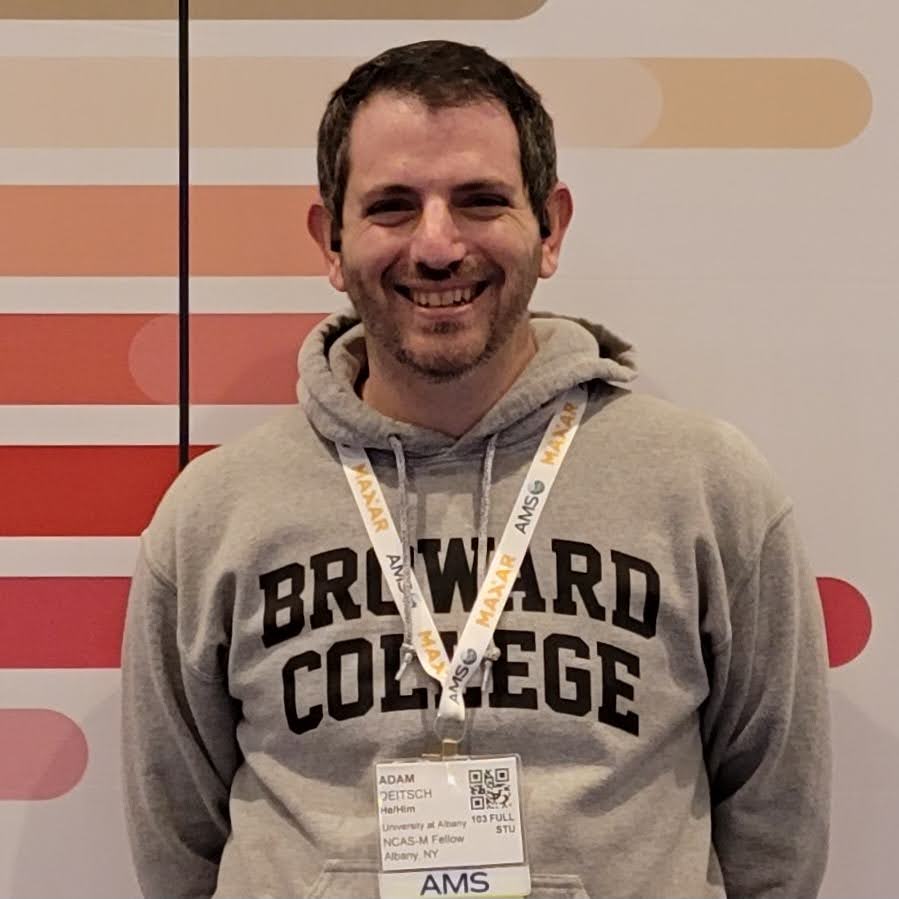 Adam Deitsch, wearing a Broward College sweatshirt and an AMS lanyard, standing in front of the #AMS2023 logo.